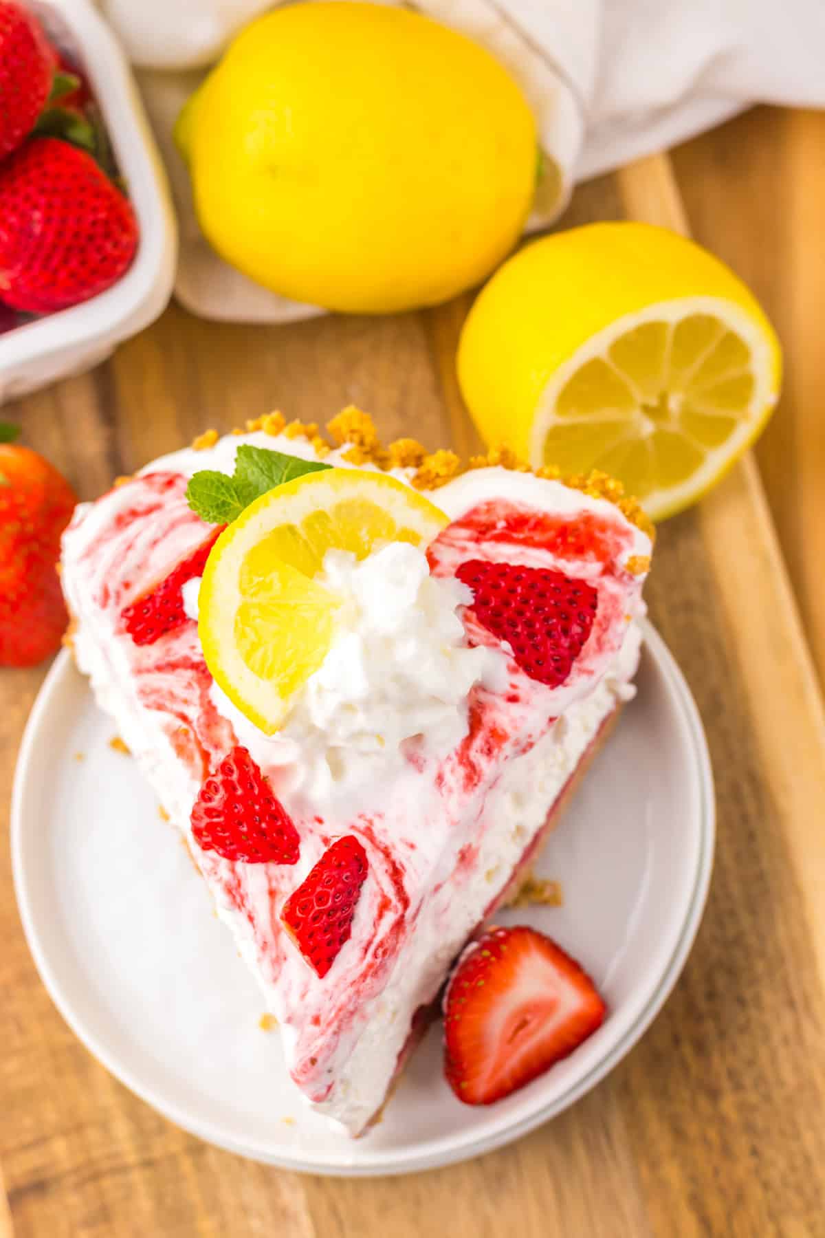 Tangy and fruity, Strawberry Lemonade Pie features layers of creamy lemonade pie filling topped with strawberry swirl. Overhead view of a slice of strawberry lemonade pie on a white plate