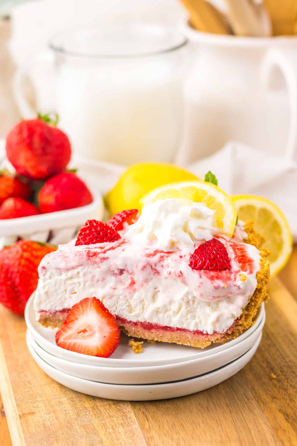 Tangy and fruity, Strawberry Lemonade Pie features layers of creamy lemonade pie filling topped with strawberry swirl. A slice of strawberry lemonade pie on a stack of white plates