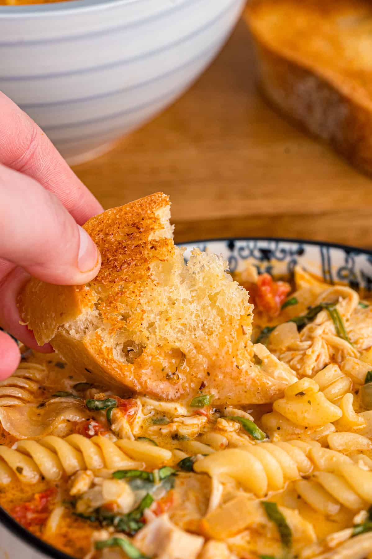 A hand dipping crusty bread into a bowl of marry me chicken soup
