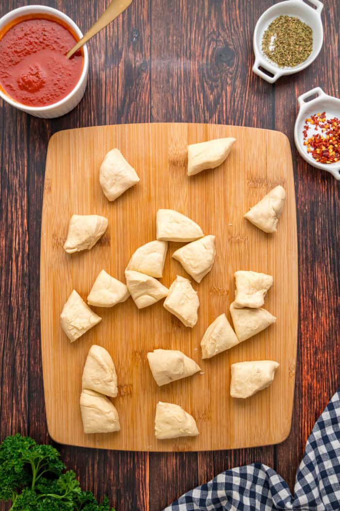 Made with biscuits, mozzarella cheese, and pepperoni, Pizza Pull Apart Bread is both easy to make and fun to eat. Biscuits cut into quarters on a cutting board