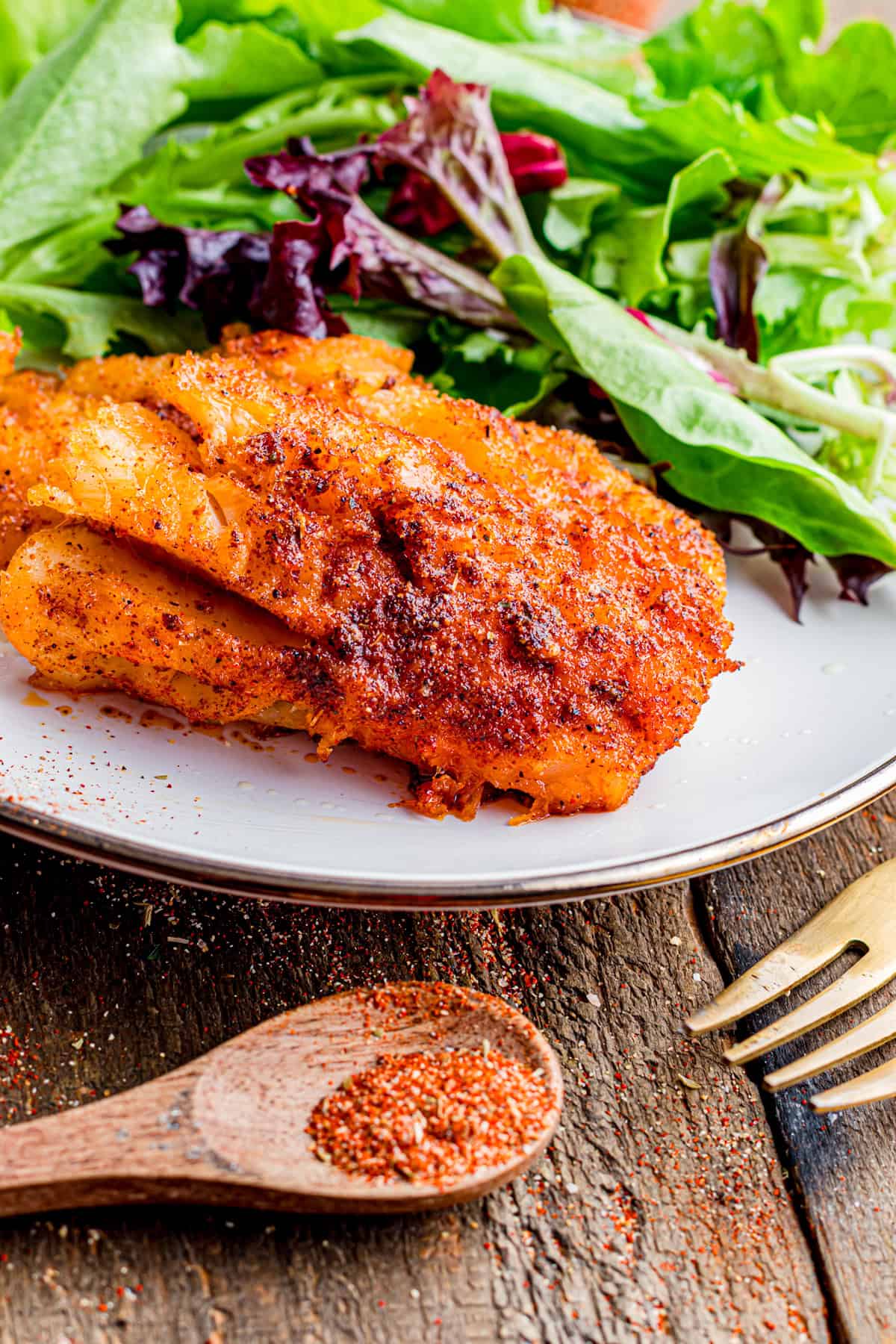 A spoon of blackened seasoning next to a plate with blackened fish