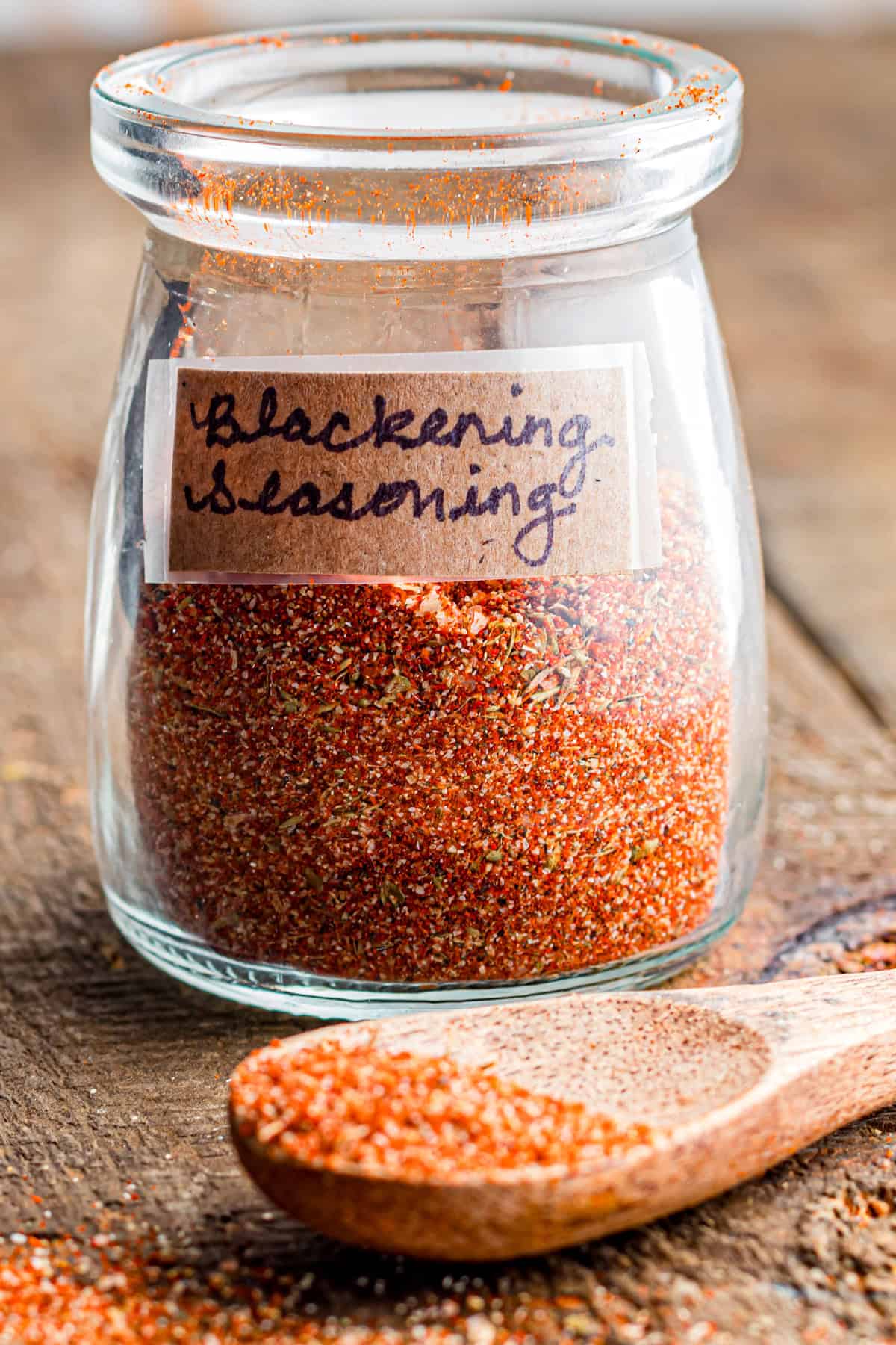 A glass jar of blackened seasoning with a wooden spoon in front