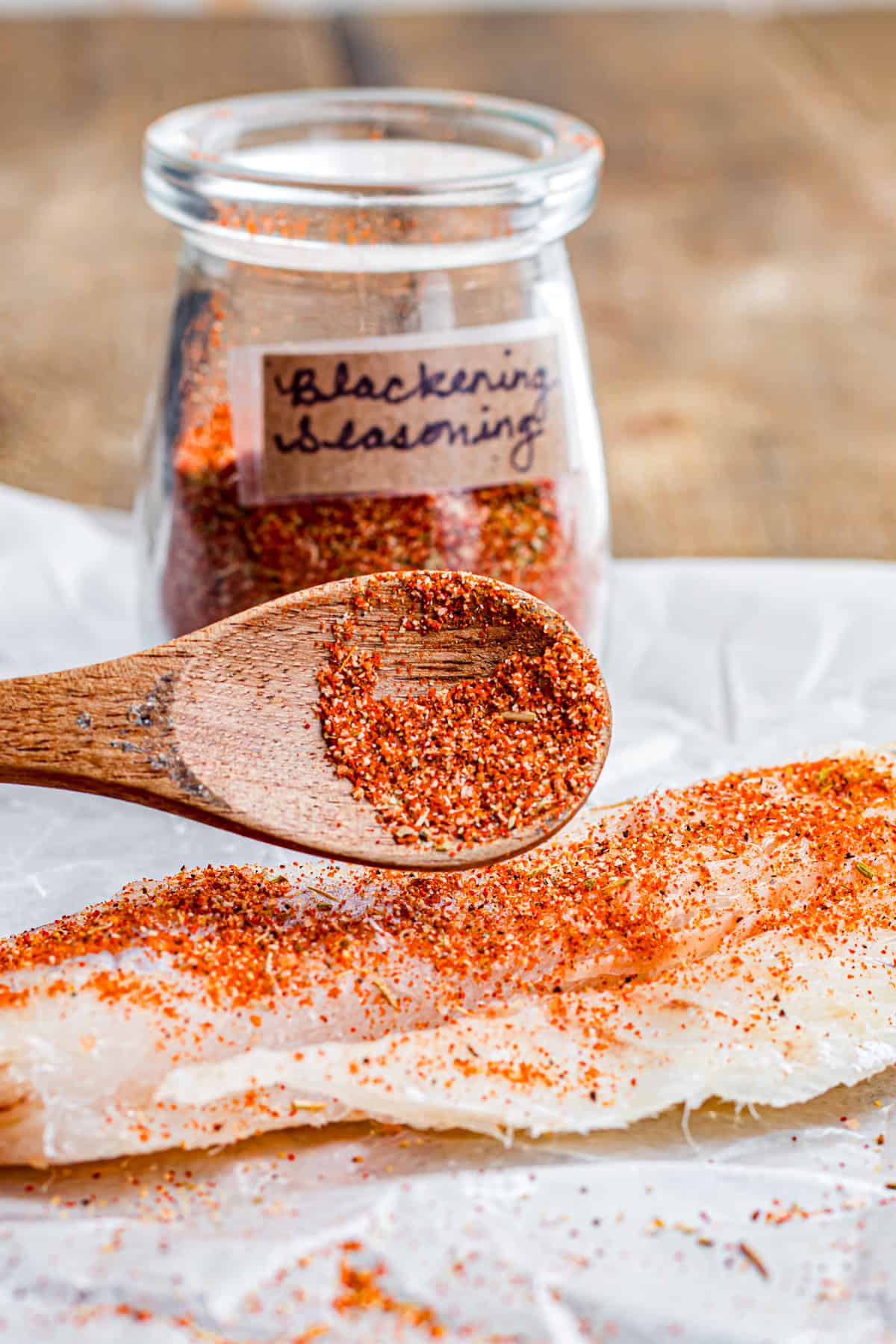 A spoon sprinkling blackened seasoning over fish