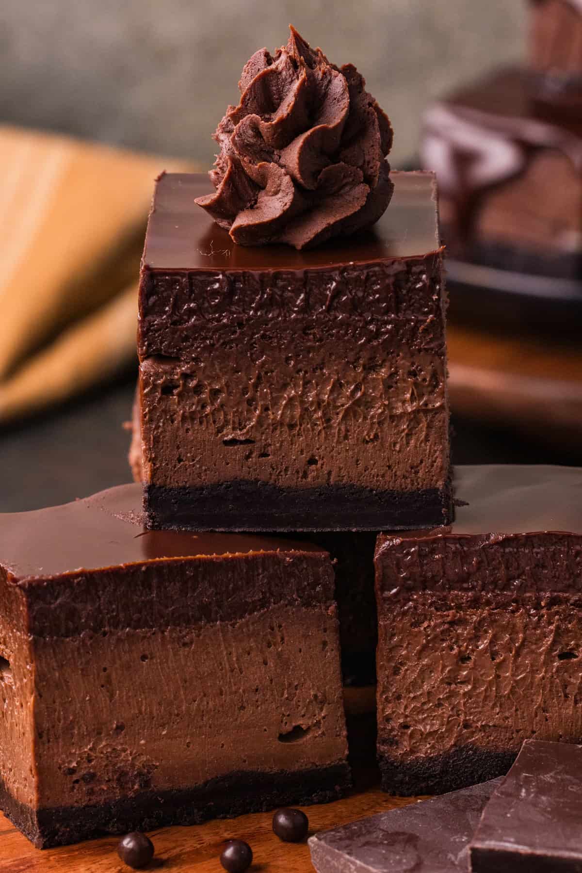 Three chocolate cheesecake bars stacked, one topped with chocolate whipped ganache