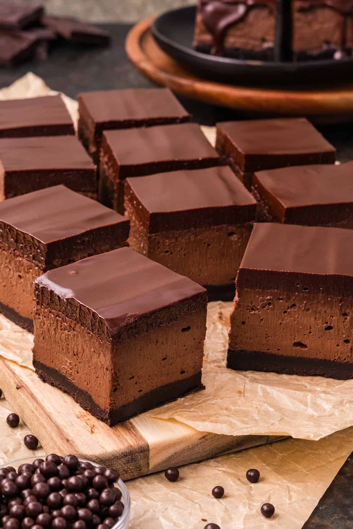 Chocolate Cheesecake Bars are ultra-decadent with three layers of chocolate. Easy to make & great for sharing! Chocolate cheesecake bars on parchment paper