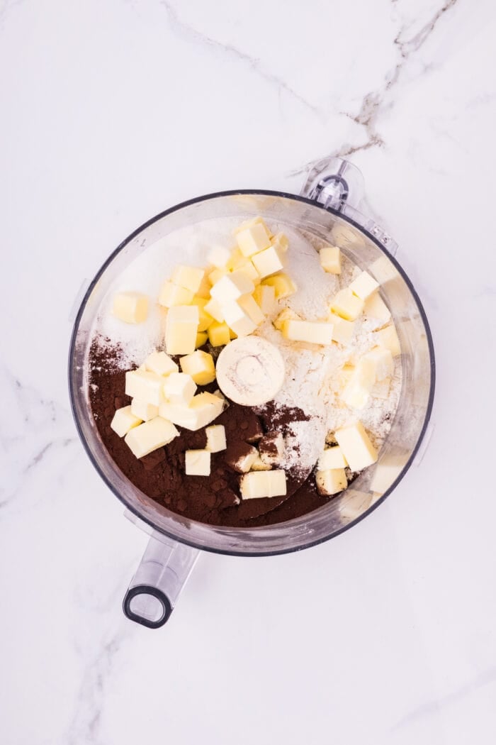 Chocolate Cheesecake Bars are ultra-decadent with three layers of chocolate. Easy to make & great for sharing! Cocoa powder, flour, and cubes of butter in a food processor