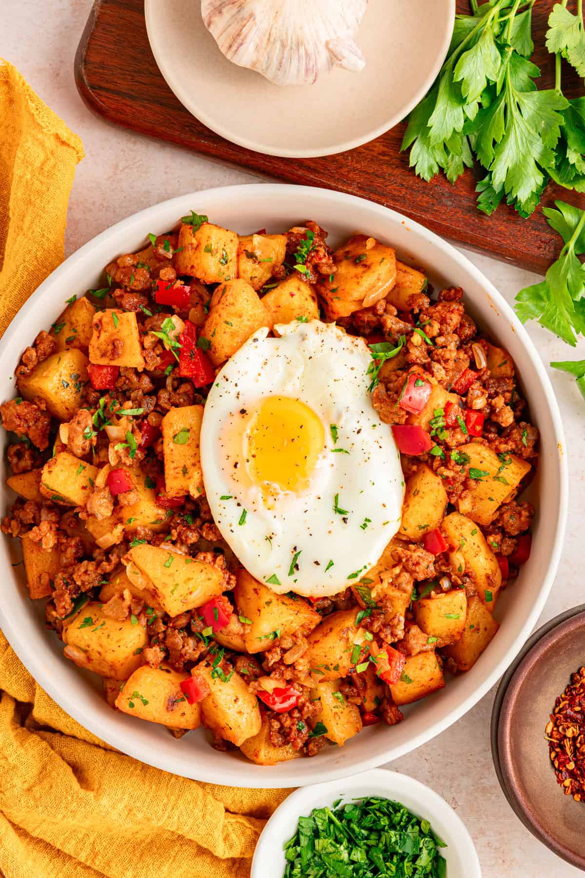Overhead view of a white bowl of chorizo and potatoes topped iwth egg