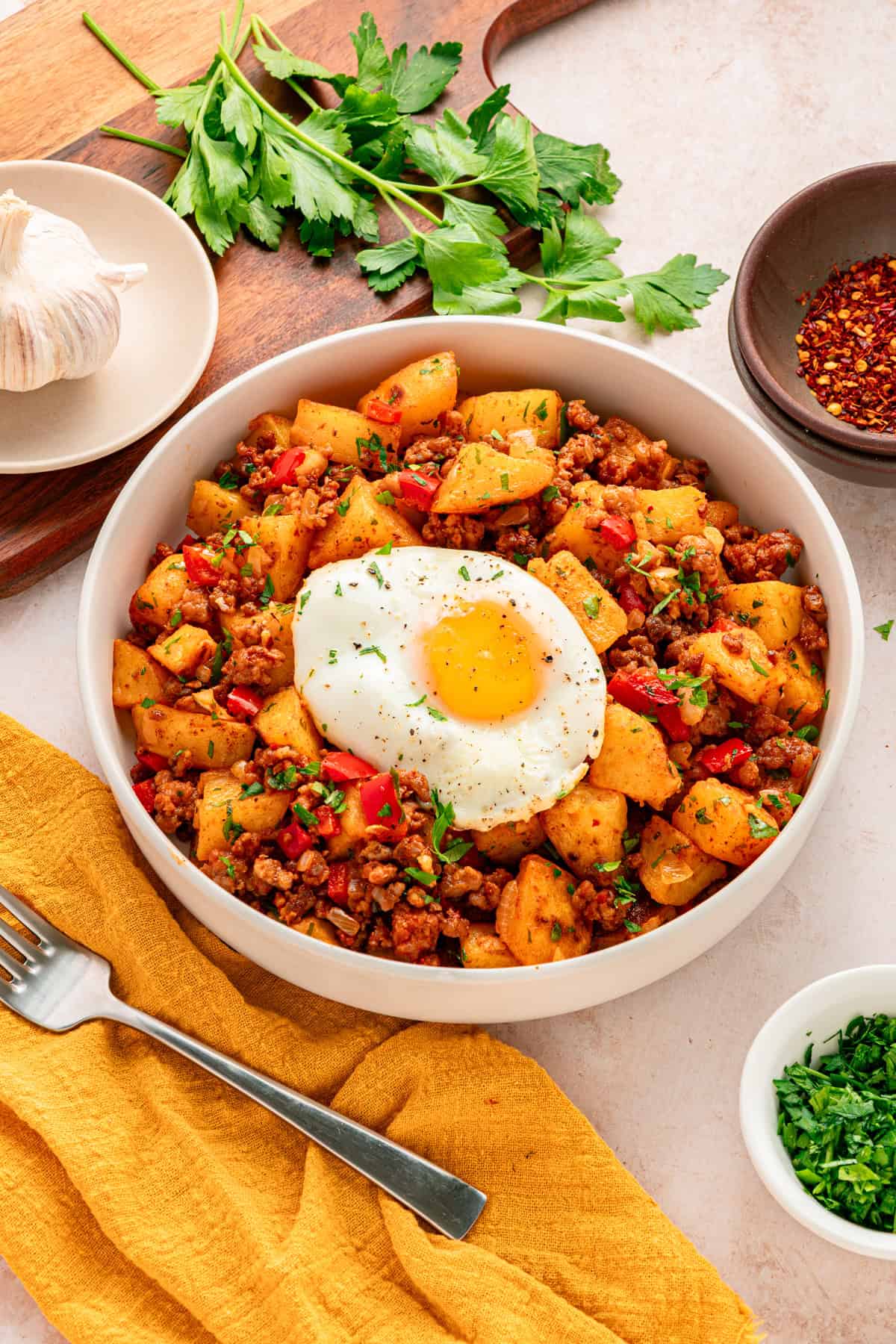 A white bowl of chorizo and potatoes topped with an egg