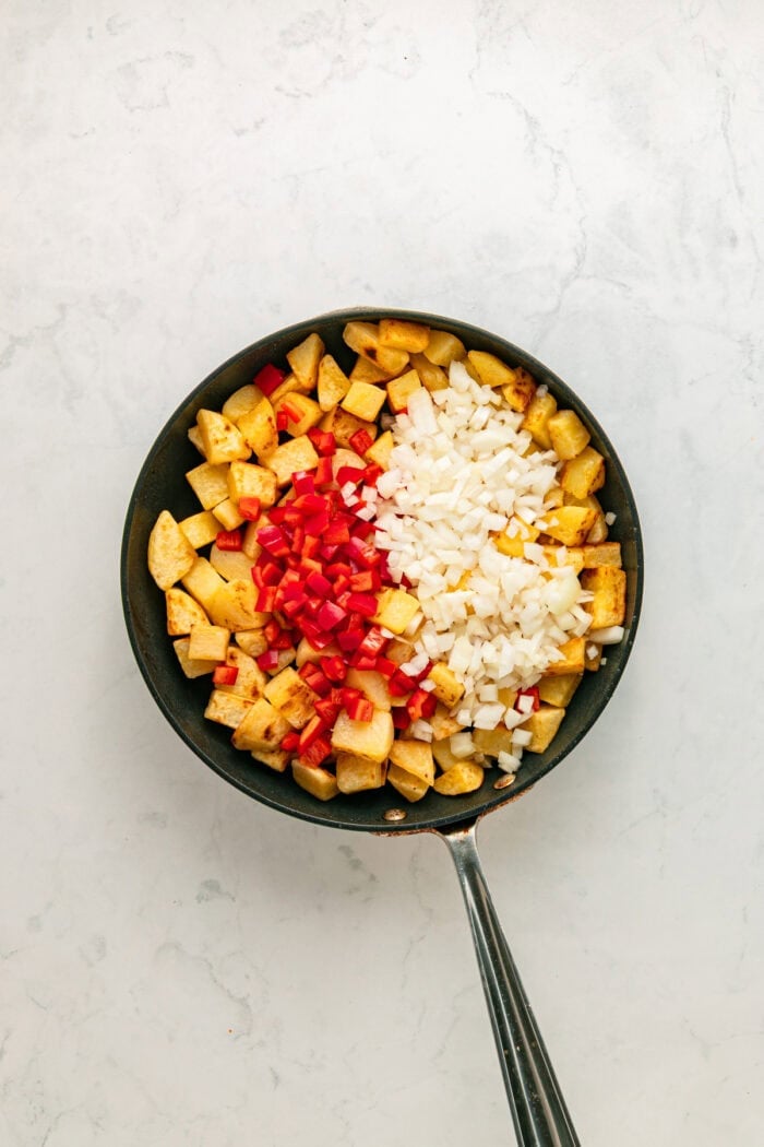 Diced pepper and onion added to crispy potatoes in a skillet