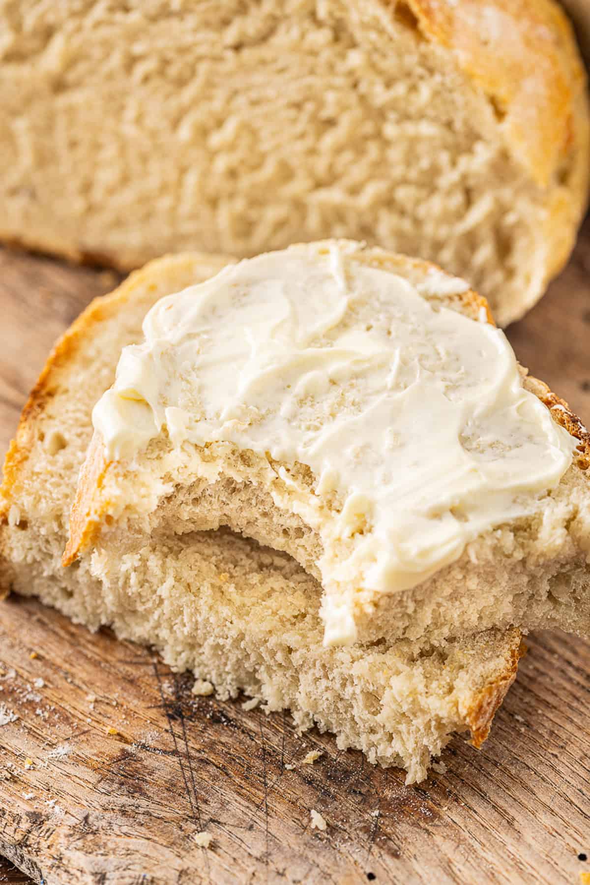 Make a crusty artisan loaf of bread at home with just 10 minutes of prep with this No Knead Dutch Oven Bread recipe. Just 4 ingredients! Two slices of Dutch oven bread, one with butter and a bite missing