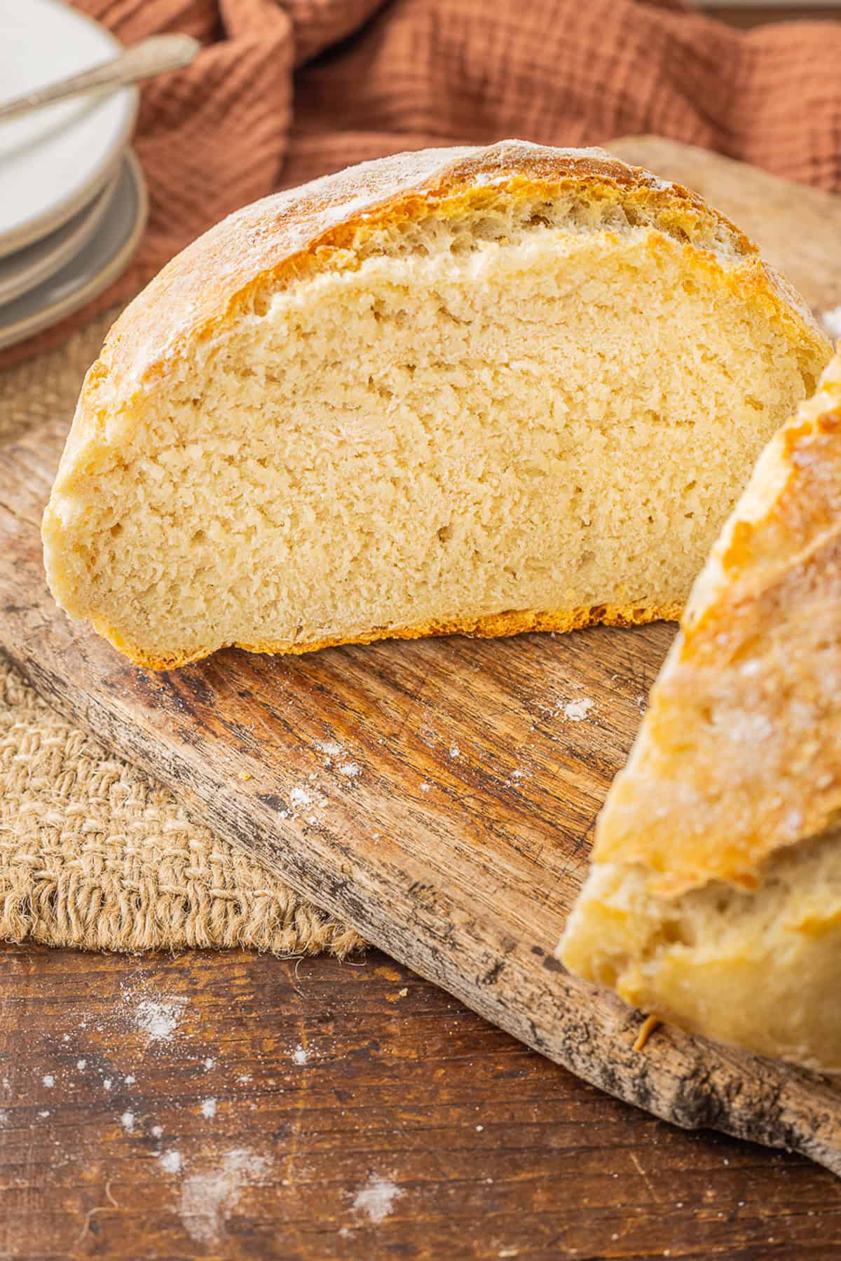 Make a crusty artisan loaf of bread at home with just 10 minutes of prep with this No Knead Dutch Oven Bread recipe. Just 4 ingredients! A loaf of Dutch oven bread cut in half on a wooden cutting board