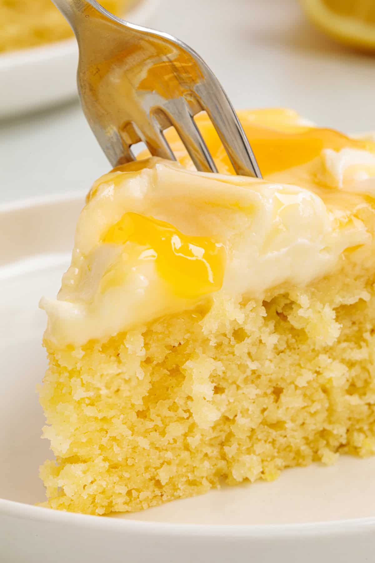 This Limoncello Mascarpone Cake begins with a moist lemon cake topped with limoncello syrup, mascarpone cream, and lemon curd. A fork cutting into Limoncello Mascarpone Cake