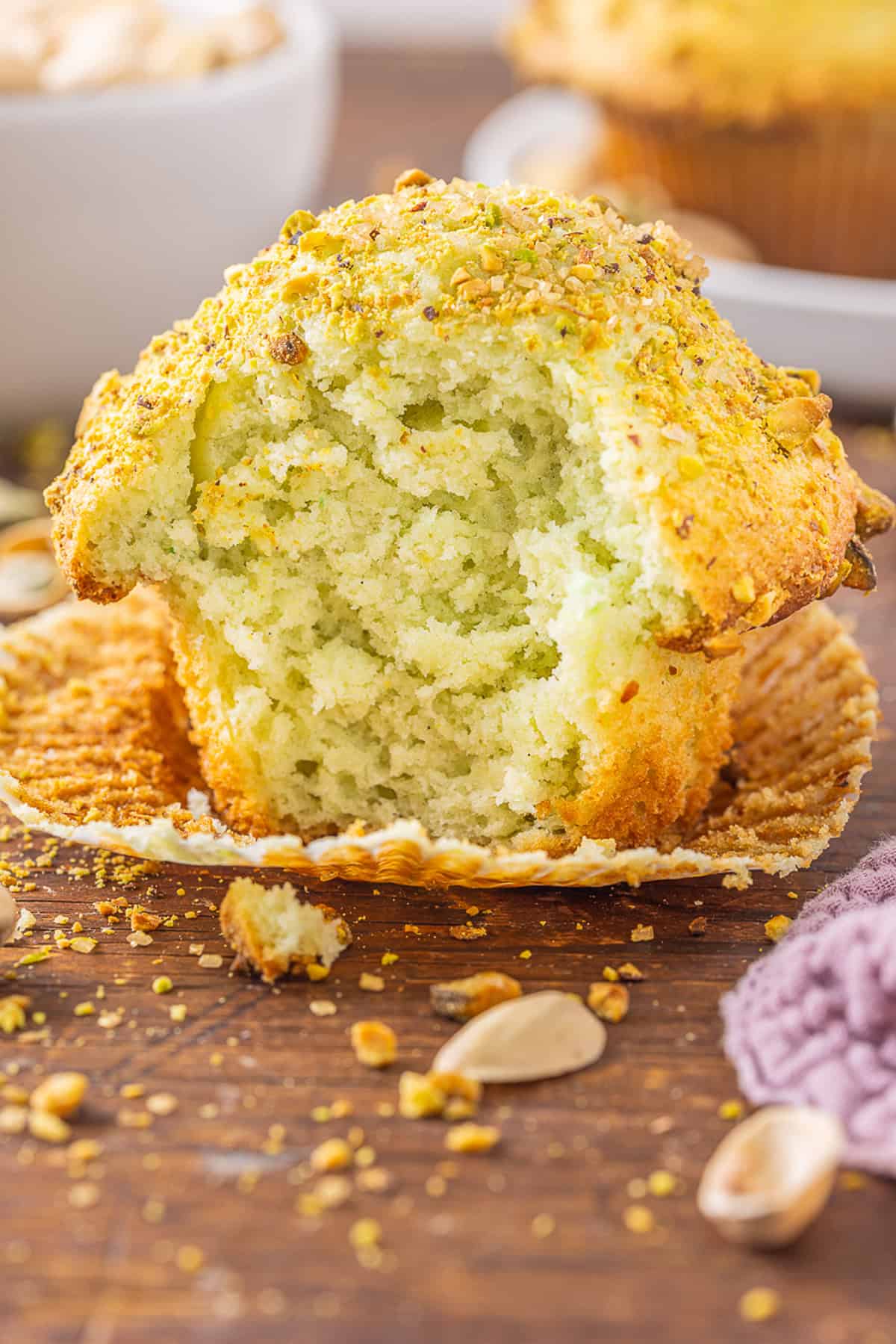 With tall bakery-style domes, these Pistachio Muffins are tender and moist with a lovely pistachio flavor. Quick & easy! A pistachio muffin with the wrapper pulled down and a bite missing
