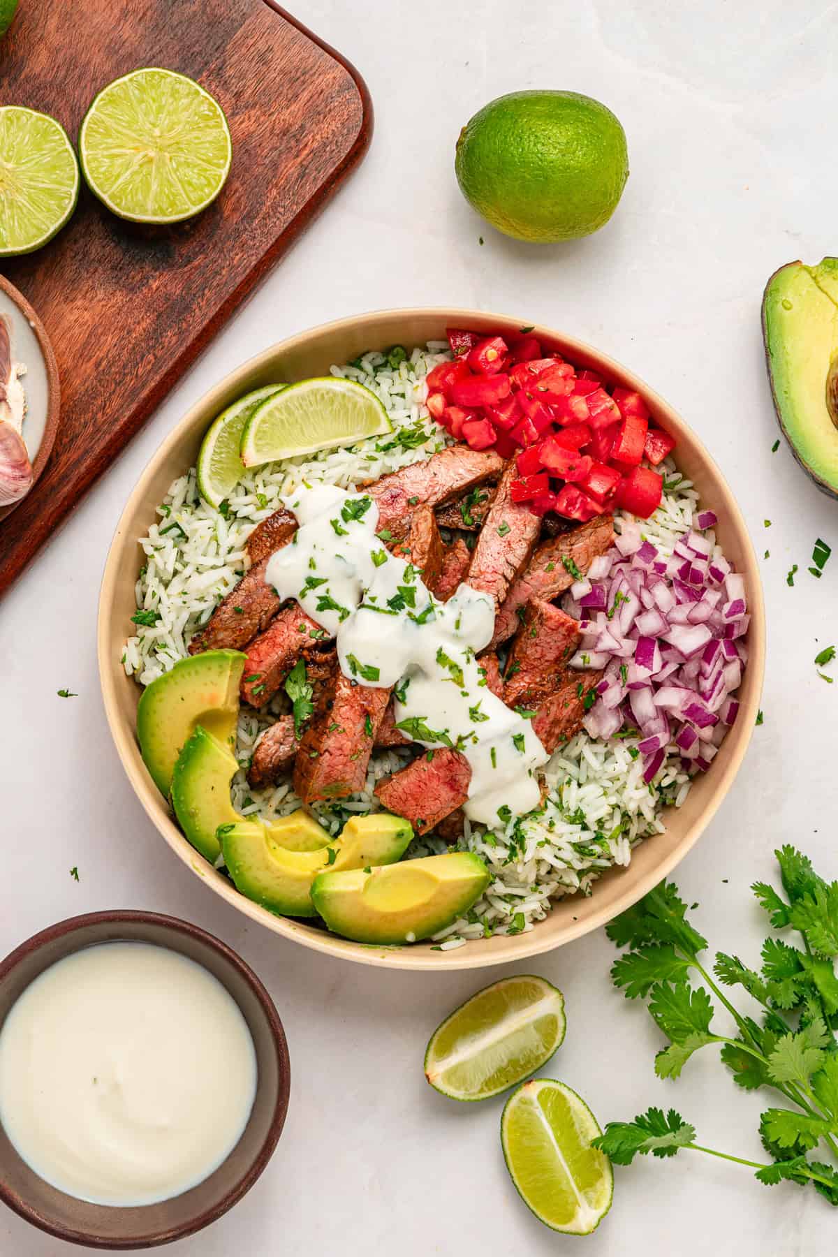 A bed of rice is topped with juicy, lightly charred flank steak, creamy yogurt lime drizzle, and veggies in this Steak Rice Bowl recipe. Overhead view of a steak rice bowl