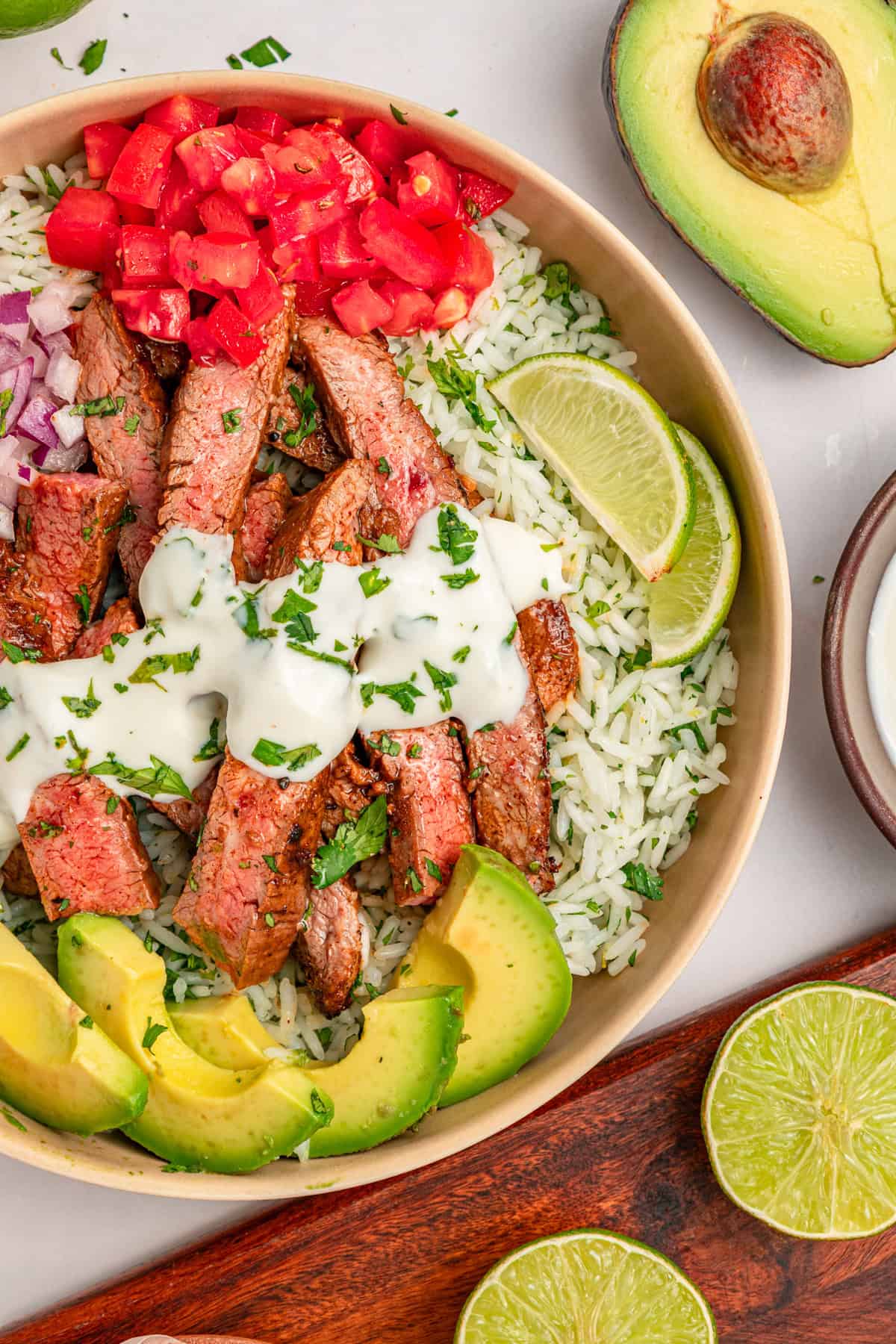 A bed of rice is topped with juicy, lightly charred flank steak, creamy yogurt lime drizzle, and veggies in this Steak Rice Bowl recipe. Overhead view of a steak rice bowl