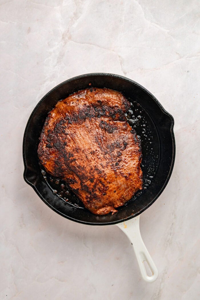 A bed of rice is topped with juicy, lightly charred flank steak, creamy yogurt lime drizzle, and veggies in this Steak Rice Bowl recipe. Seared flank steak in a cast iron skillet