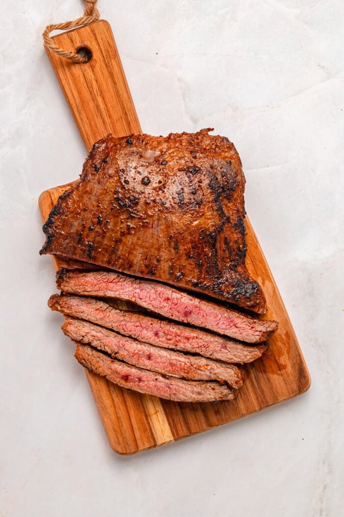 A bed of rice is topped with juicy, lightly charred flank steak, creamy yogurt lime drizzle, and veggies in this Steak Rice Bowl recipe. Sliced flank steak on a cutting board