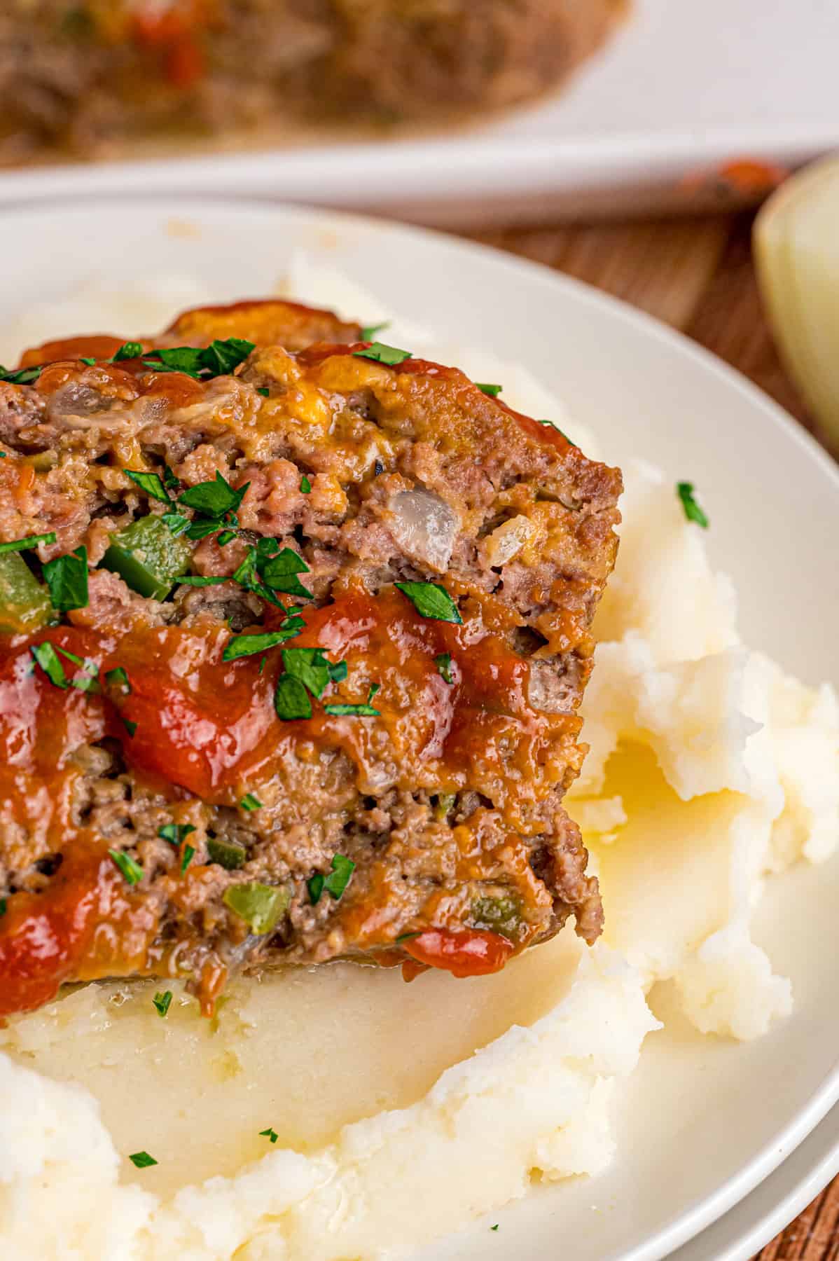 Shredded cheddar, sauteed onions and bell peppers, and Ritz cracker crumbs make this Cracker Barrel Meatloaf extra moist and flavorful. A slice of Cracker Barrel meatloaf over mashed potatoes on a plate