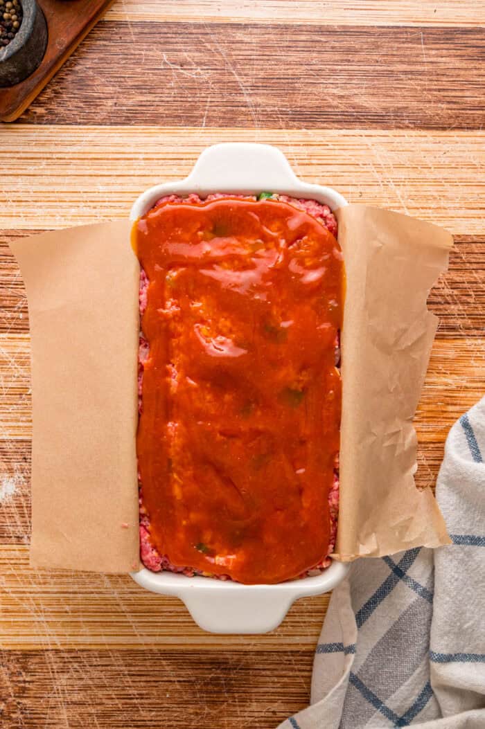 Shredded cheddar, sauteed onions and bell peppers, and Ritz cracker crumbs make this Cracker Barrel Meatloaf extra moist and flavorful. Ketchup glaze over meatloaf in a loaf pan
