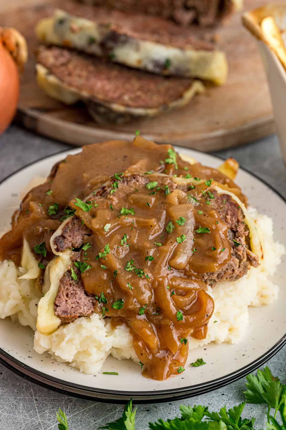 Caramelized onions, a savory onion sauce, and gooey, cheese turn basic meatloaf into an elevated dinner in this French Onion Meatloaf recipe. A plate of French onion meatloaf with mashed potatoes