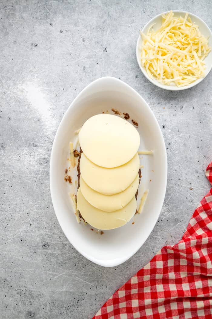 Caramelized onions, a savory onion sauce, and gooey, cheese turn basic meatloaf into an elevated dinner in this French Onion Meatloaf recipe. Slices of provolone cheese over meatloaf in a baking dish