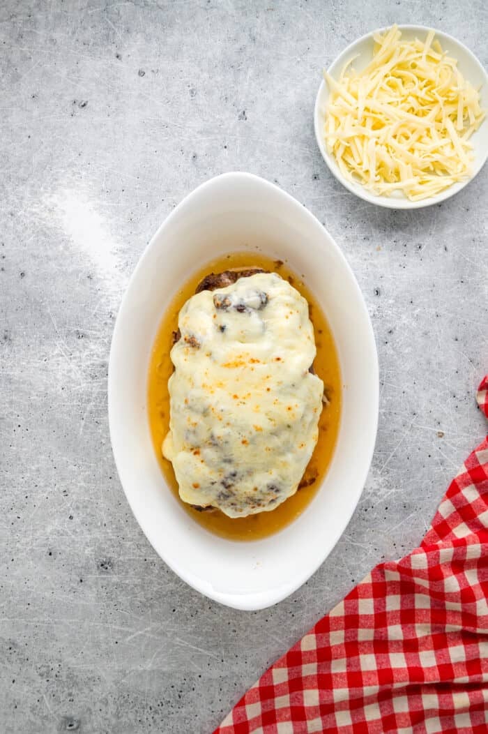 Caramelized onions, a savory onion sauce, and gooey, cheese turn basic meatloaf into an elevated dinner in this French Onion Meatloaf recipe. Melted cheese on meatloaf in a baking dish