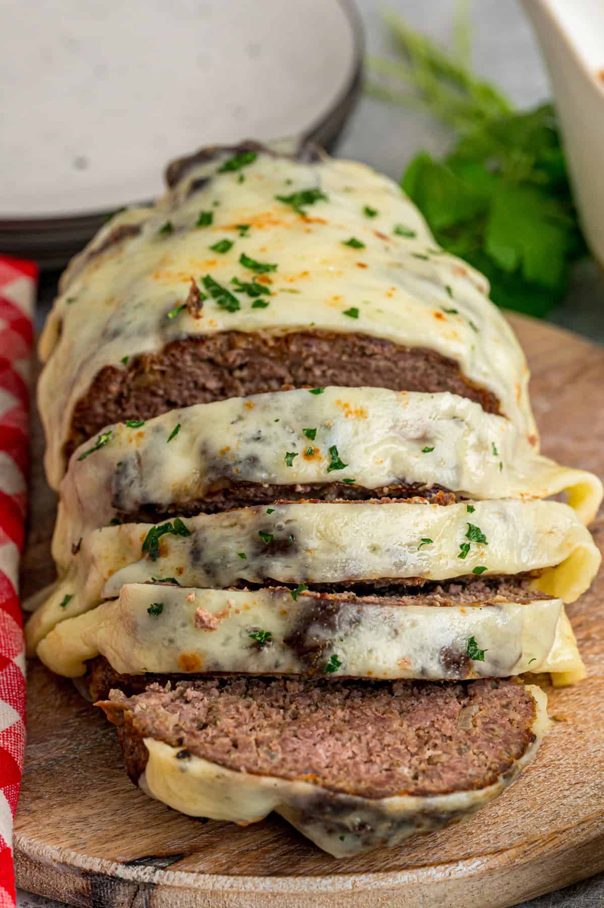 Caramelized onions, a savory onion sauce, and gooey, cheese turn basic meatloaf into an elevated dinner in this French Onion Meatloaf recipe. Front view of French onion meatloaf with several pieces sliced