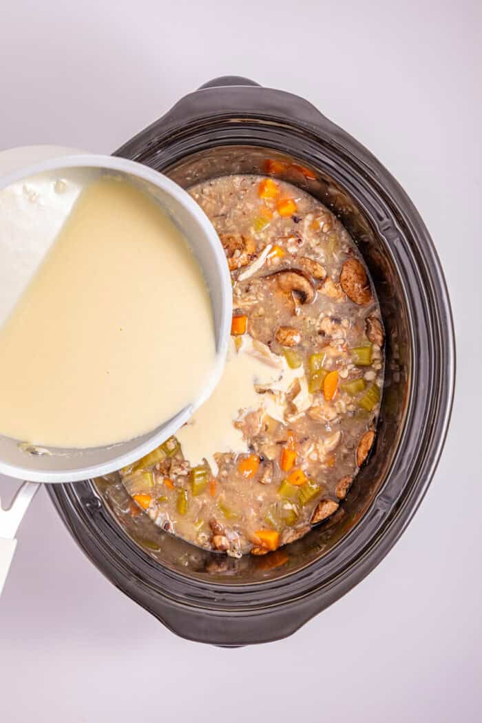 This Crock Pot Chicken Wild Rice Soup is the perfect dump & go crock pot recipe for busy weekdays. Hearty & filling. Pouring roux into the crock pot to thicken the soup