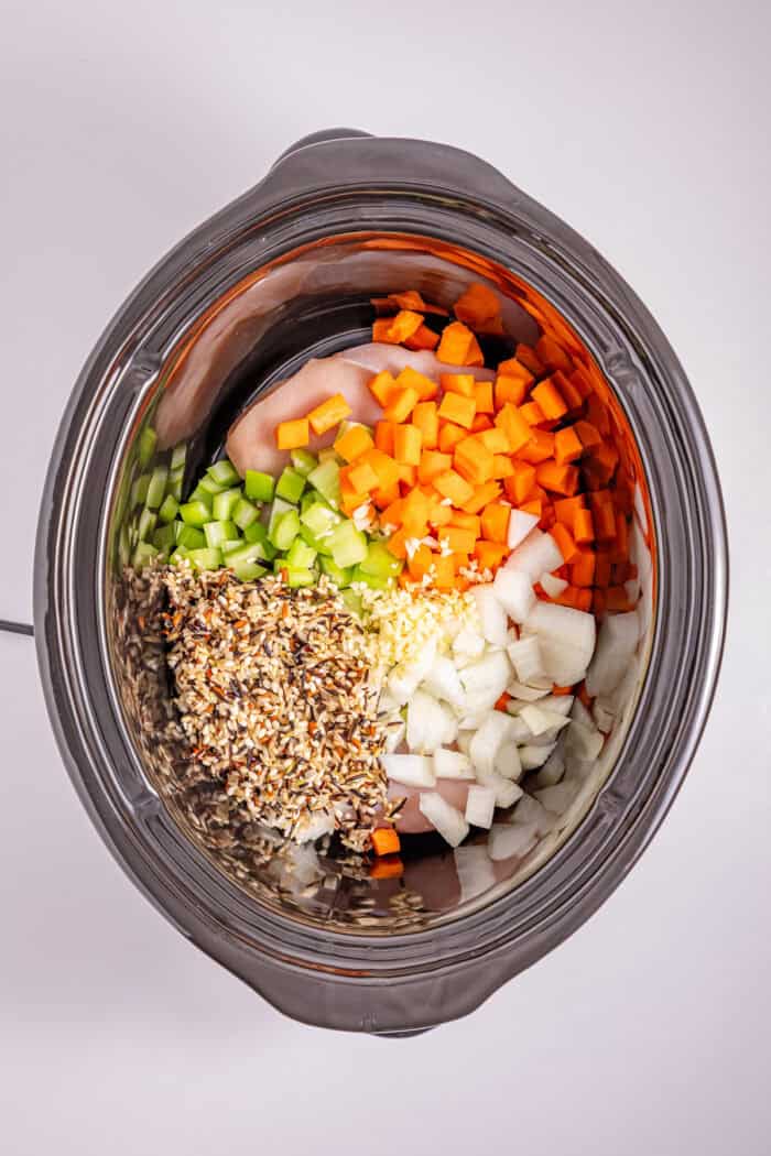 This Crock Pot Chicken Wild Rice Soup is the perfect dump & go crock pot recipe for busy weekdays. Hearty & filling. Carrots, celery, onion, and garlic on top of chicken in the crock pot