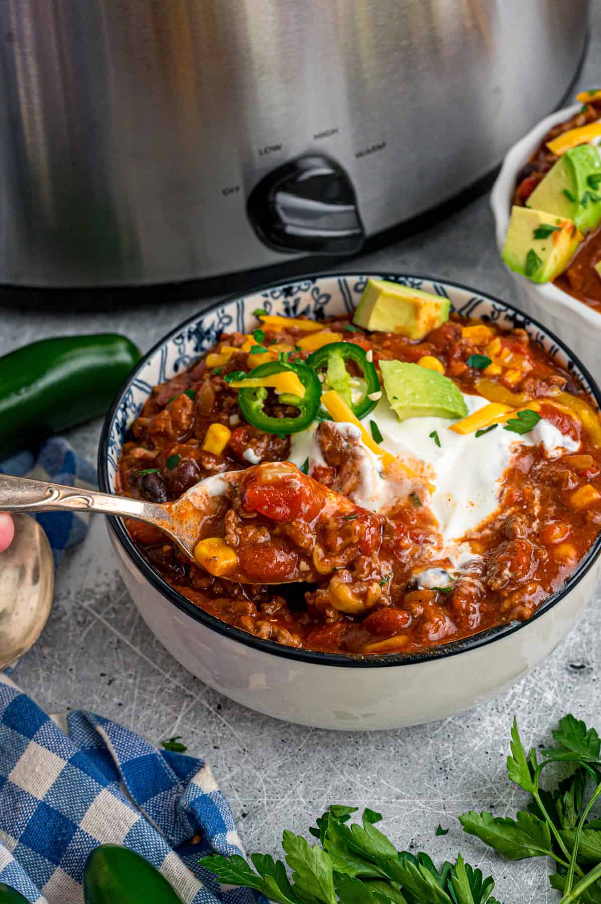 A spoon in a bowl of chili in front of the crockpot