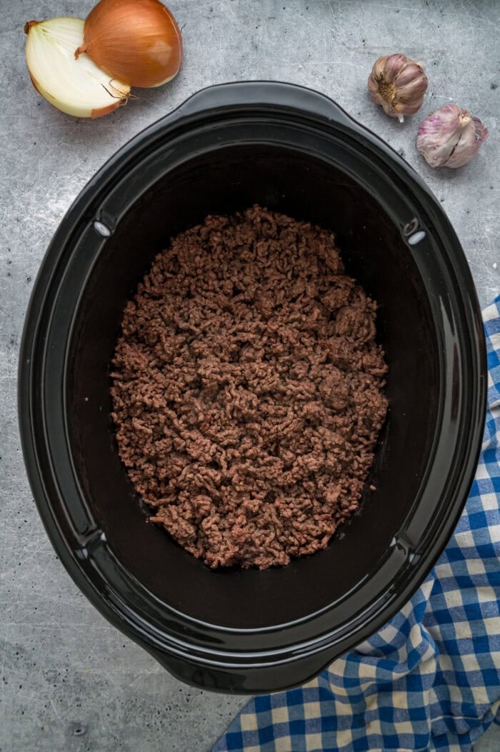Browned ground beef in the bottom of a slow cooker