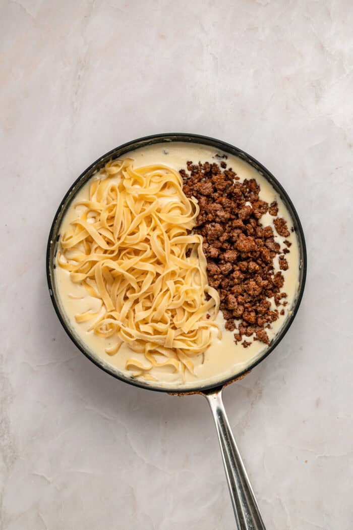 Pasta and ground beef added to a skillet of alfredo sauce