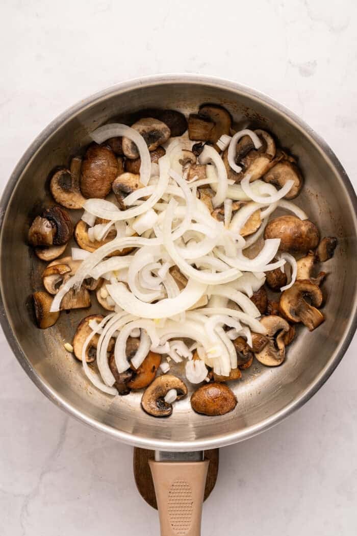 Juicy beef burgers are topped with slices of melty Swiss cheese and savory sauteed mushrooms in this Mushroom Swiss Burger recipe. Sliced onions added to mushrooms in a pan
