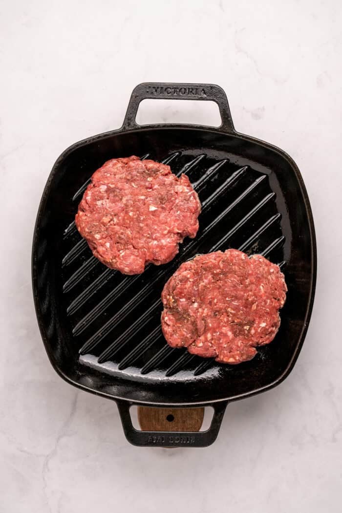 Juicy beef burgers are topped with slices of melty Swiss cheese and savory sauteed mushrooms in this Mushroom Swiss Burger recipe. Two burger patties on a grill pan