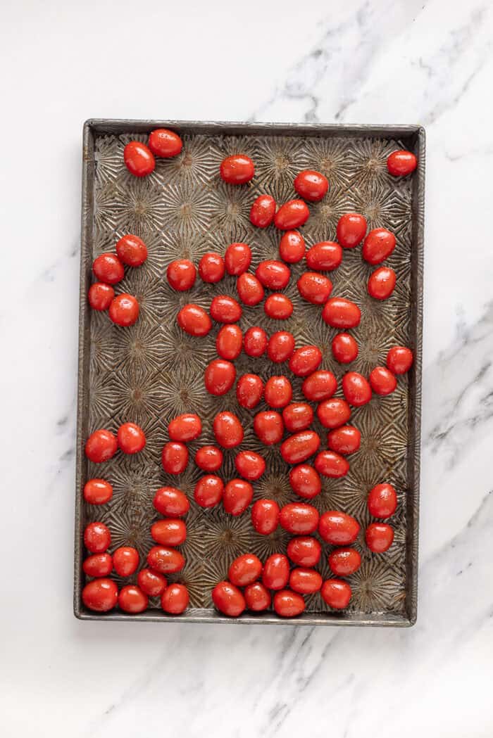 Juicy chicken breasts are cooked in a creamy pesto sauce with roasted tomatoes in this Pesto Chicken recipe. Grape tomatoes on a baking sheet