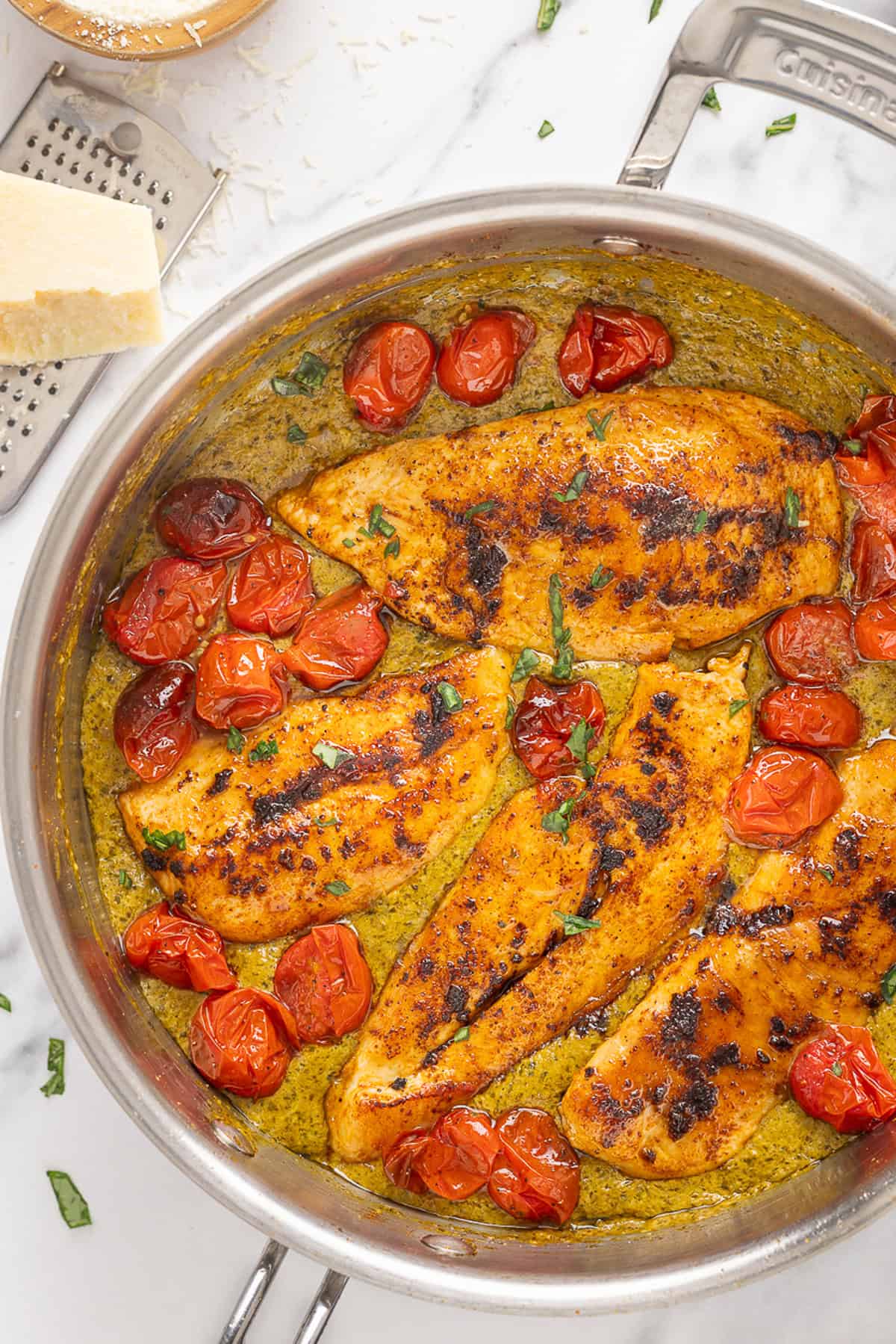 Juicy chicken breasts are cooked in a creamy pesto sauce with roasted tomatoes in this Pesto Chicken recipe. Overhead view of a pan of pesto chicken