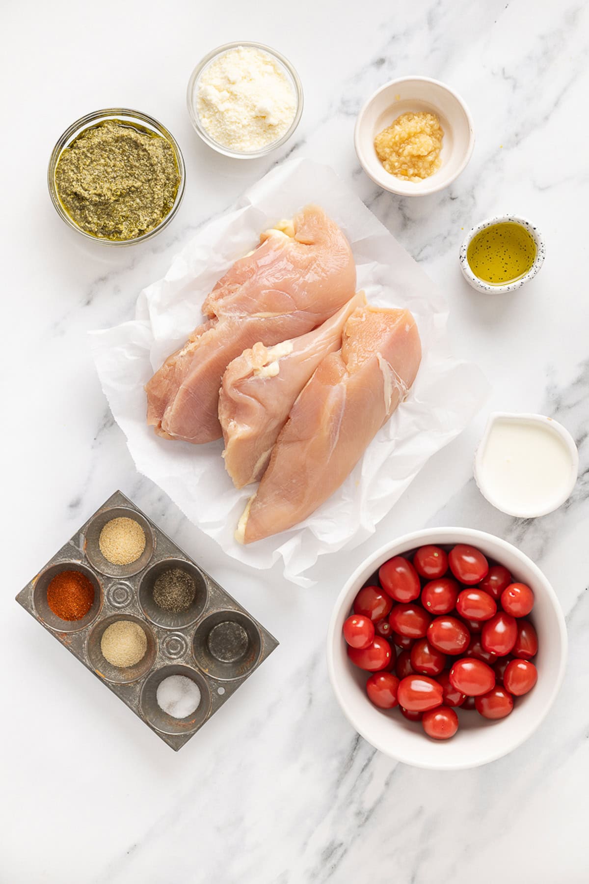 Juicy chicken breasts are cooked in a creamy pesto sauce with roasted tomatoes in this Pesto Chicken recipe. Overhead view of ingredients needed to make pesto chicken