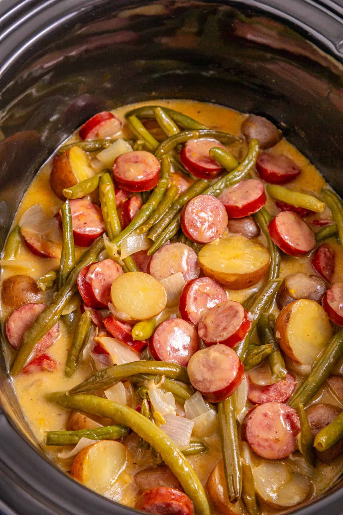 Baby potatoes, smoked sausage, and green beans are slow-cooked in Cajun seasoning and cream of chicken soup in this Crockpot Swamp Potatoes recipe. It’s an easy, flavorful dump-and-go recipe that’s perfect for busy weekends. Overhead view of swamp potatoes in a crockpot