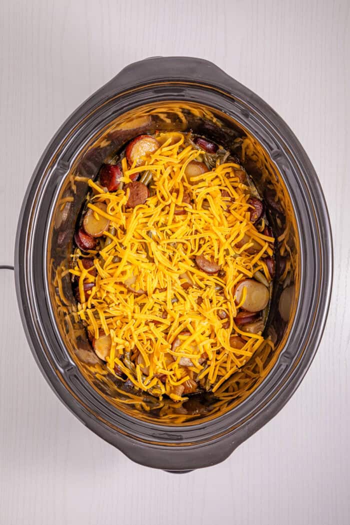 Baby potatoes, smoked sausage, and green beans are slow-cooked in Cajun seasoning and cream of chicken soup in this Crockpot Swamp Potatoes recipe. It’s an easy, flavorful dump-and-go recipe that’s perfect for busy weekends. Shredded cheddar on top of green beans, sausage, and potatoes in a crockpot