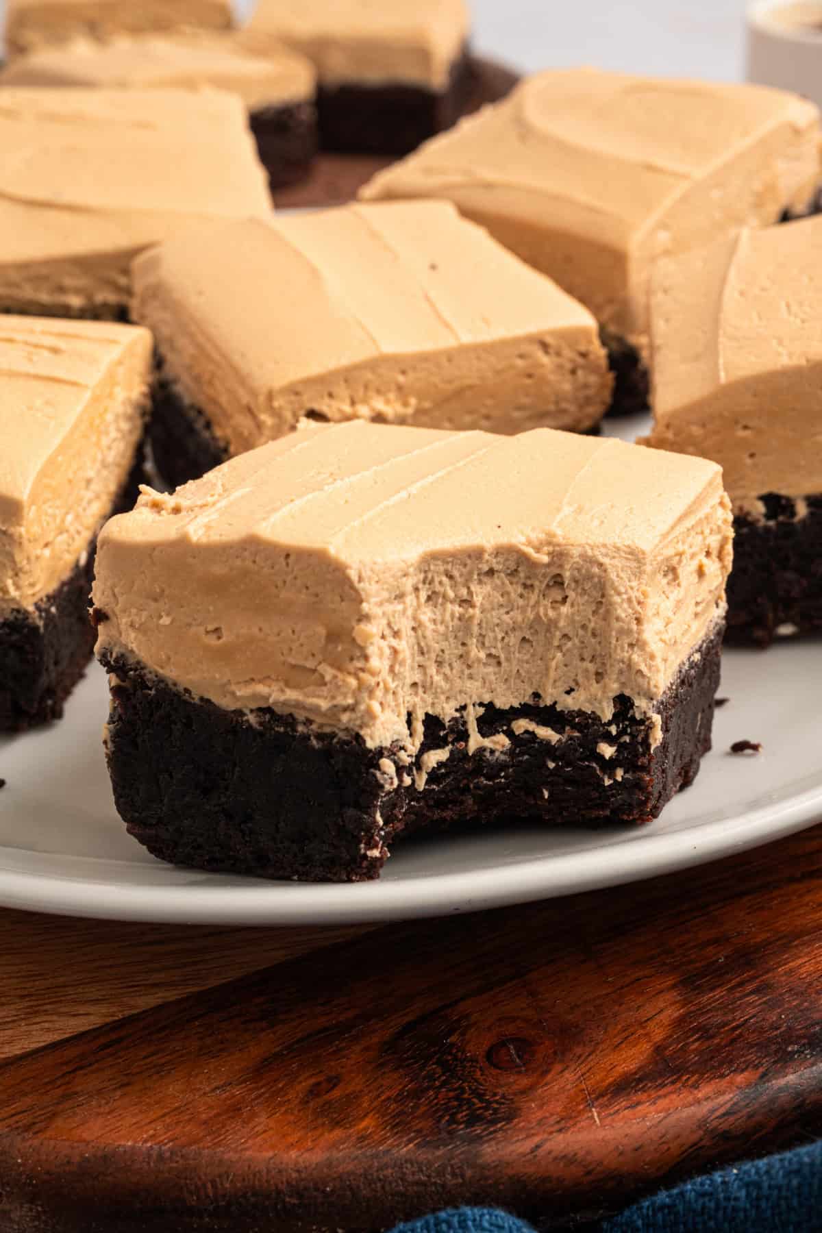 Espresso Brownies feature fudgy, dense chocolate brownies with a hint of espresso, topped with a layer of espresso buttercream frosting. Espresso Brownies with a bite take out on a plate