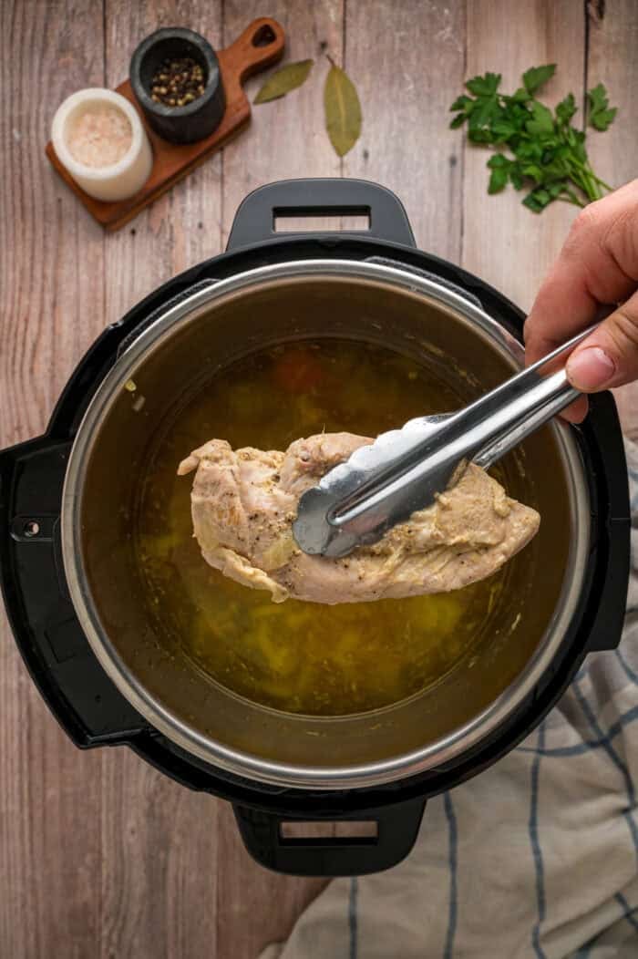 With egg noodles, shredded chicken, carrots, and celery, this Instant Pot Chicken Noodle Soup is classic comfort food made quick and easy. Tongs removing cooked chicken from the Instant Pot