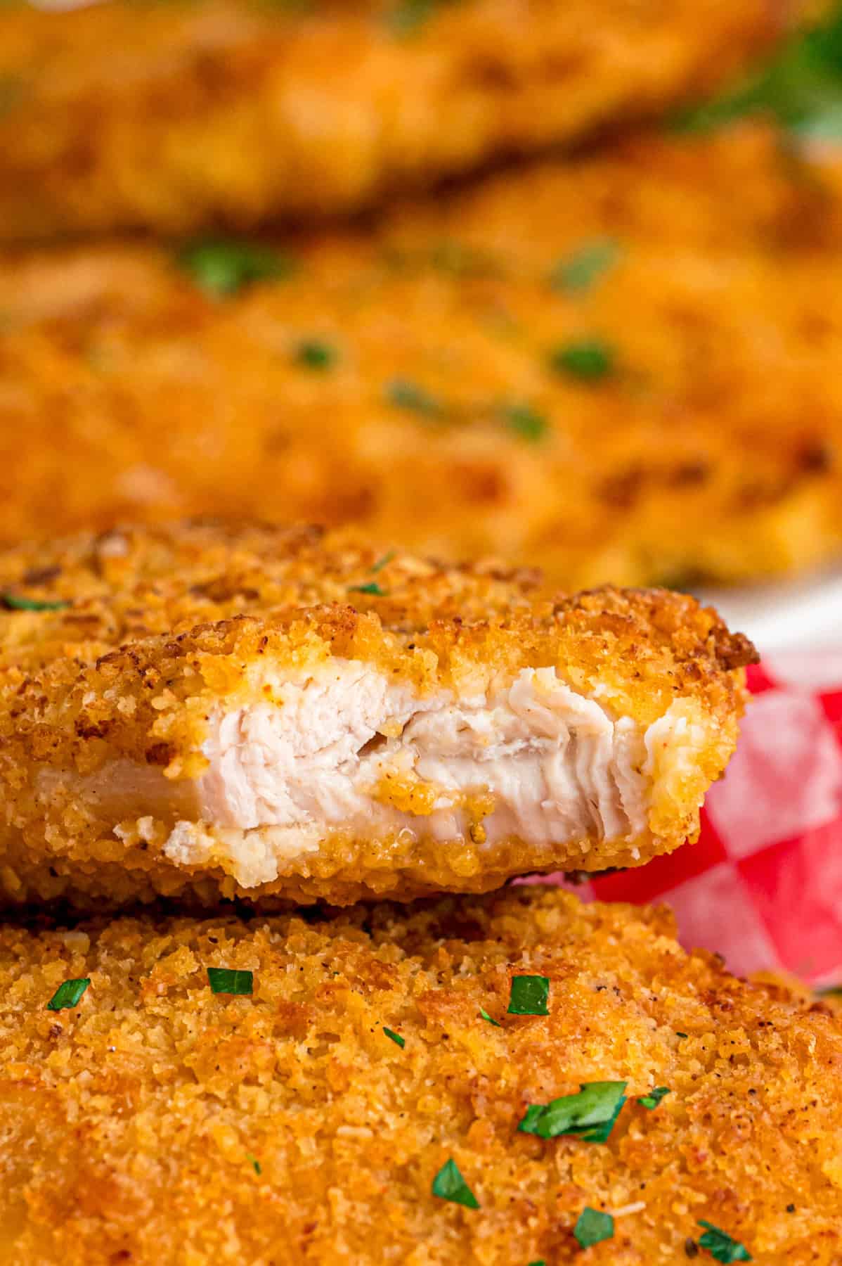 Coated in seasoned panko breadcrumbs, this oven fried chicken is crispy on the outside and juicy on the inside. Quick & easy! Two pieces of oven fried chicken, one with a bite missing to show the juicy inside