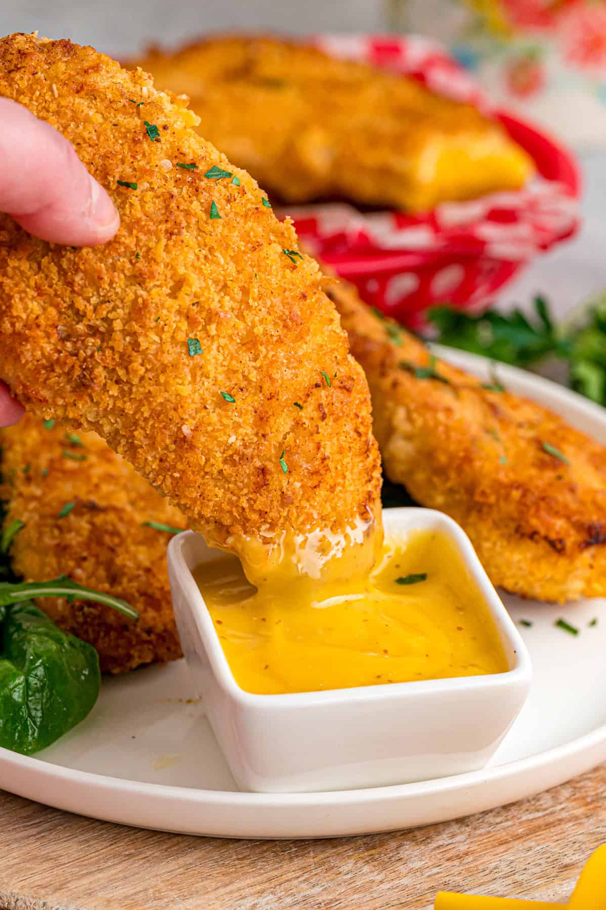 Coated in seasoned panko breadcrumbs, this oven fried chicken is crispy on the outside and juicy on the inside. Quick & easy! A hand dipping oven fried chicken into honey mustard