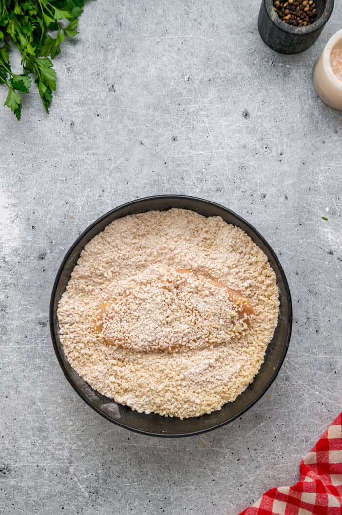 Coated in seasoned panko breadcrumbs, this oven fried chicken is crispy on the outside and juicy on the inside. Quick & easy! A chicken strip in a bowl of breadcrumbs