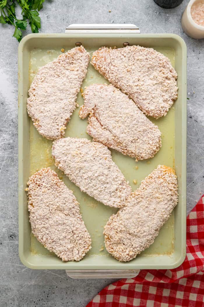 Coated in seasoned panko breadcrumbs, this oven fried chicken is crispy on the outside and juicy on the inside. Quick & easy! Pieces of breaded chicken on a baking sheet