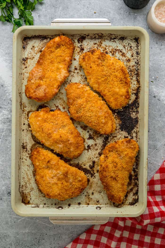Coated in seasoned panko breadcrumbs, this oven fried chicken is crispy on the outside and juicy on the inside. Quick & easy! Overhead view of oven fried chicken on a baking sheet