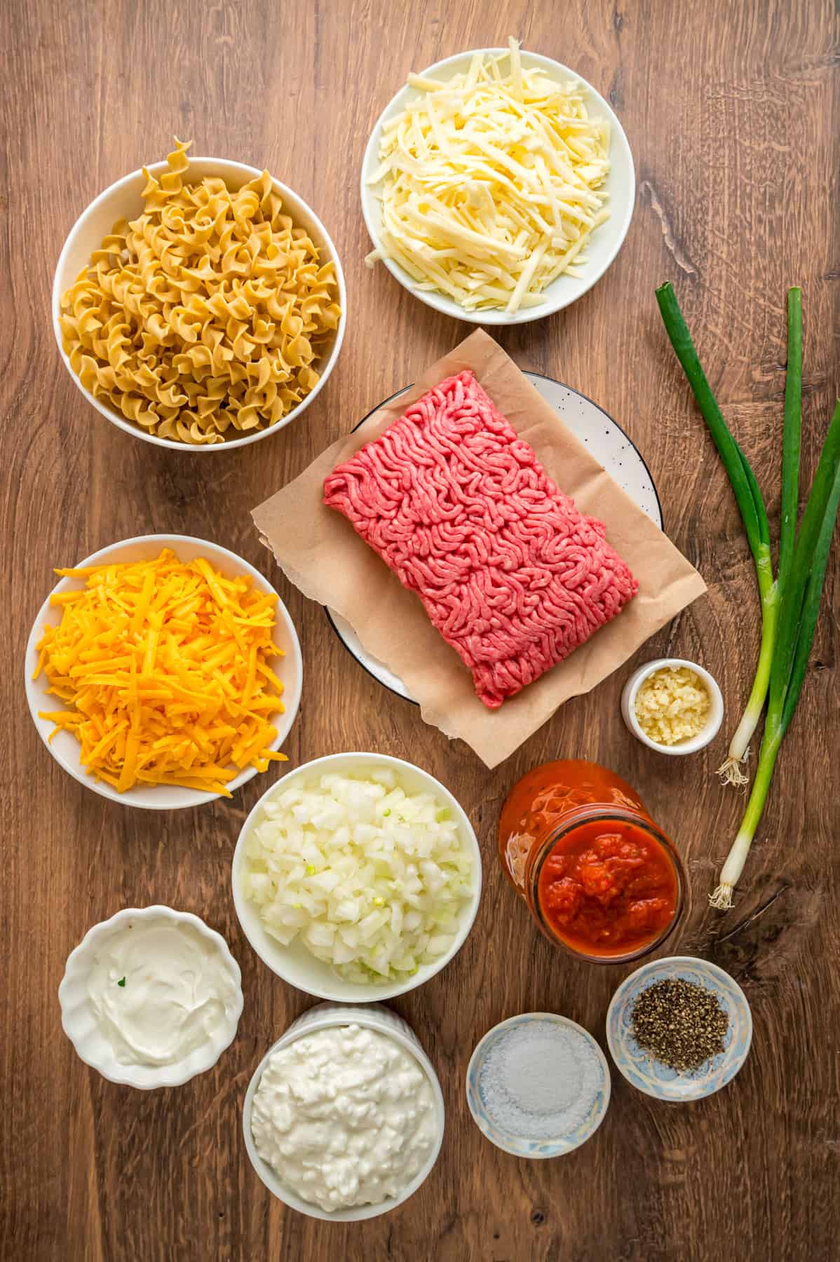 With noodles coated in sour cream, meat sauce, and lots of cheese, this sour cream noodle bake is quick, easy & comforting. Overhead view of ingredients needed to make sour cream noodle bake