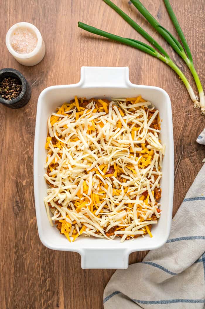 With noodles coated in sour cream, meat sauce, and lots of cheese, this sour cream noodle bake is quick, easy & comforting. Cheese covering the meat sauce in a baking dish