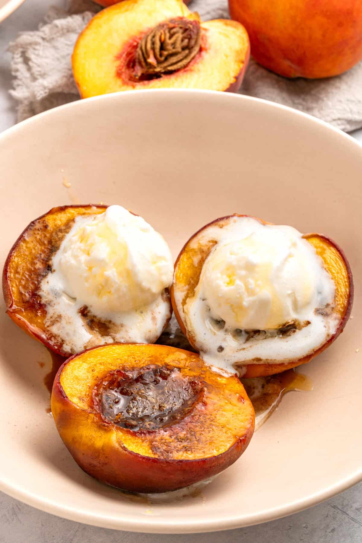 Three baked peach halves in a bowl with ice cream