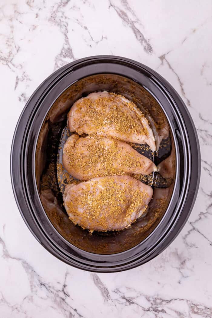 Chicken breast is slow cooked in salsa verde then shredded to make this Crockpot Salsa Verde Chicken. Easy dinner idea! Seasoned chicken breasts in the bottom of a slow cooker